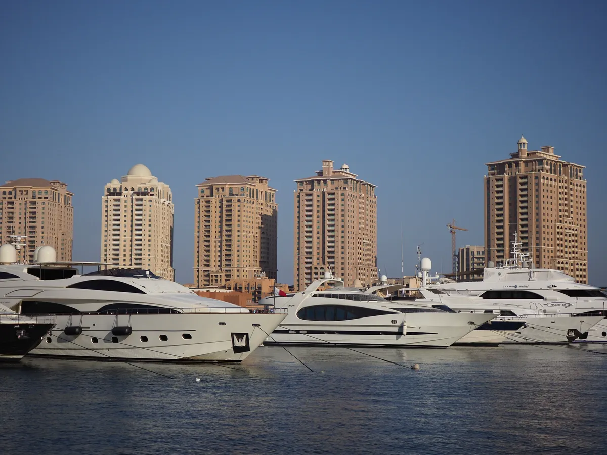White motor yachts moored side by side in a marina, with beige high-rise towers behind them under a clear blue sky.